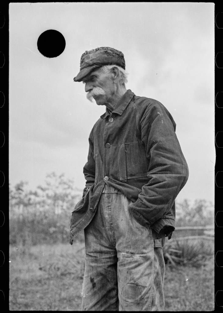 Older worker in worn jacket and cap
